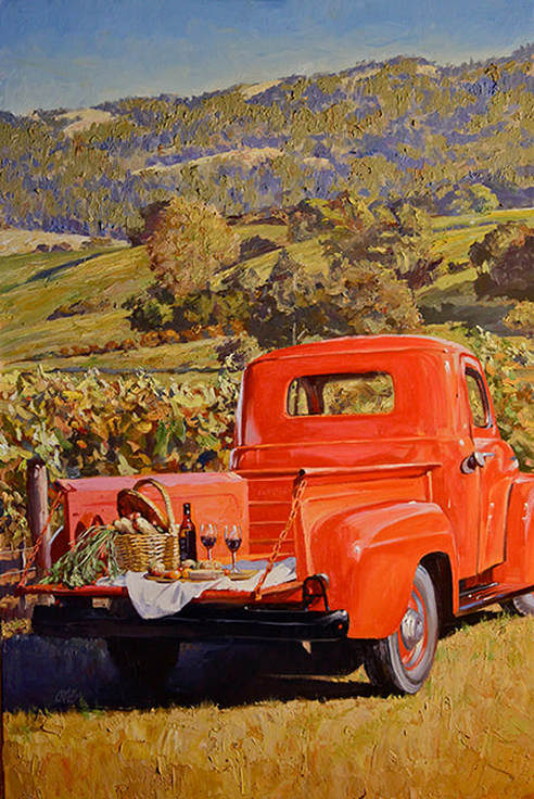 Classic red truck with picnic on tail bed in front of vineyard landscape