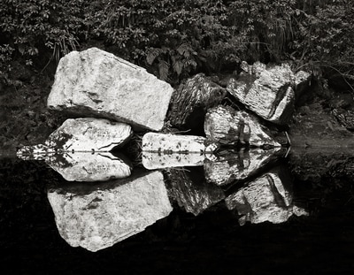 Black and white photograph of boulders reflected in river